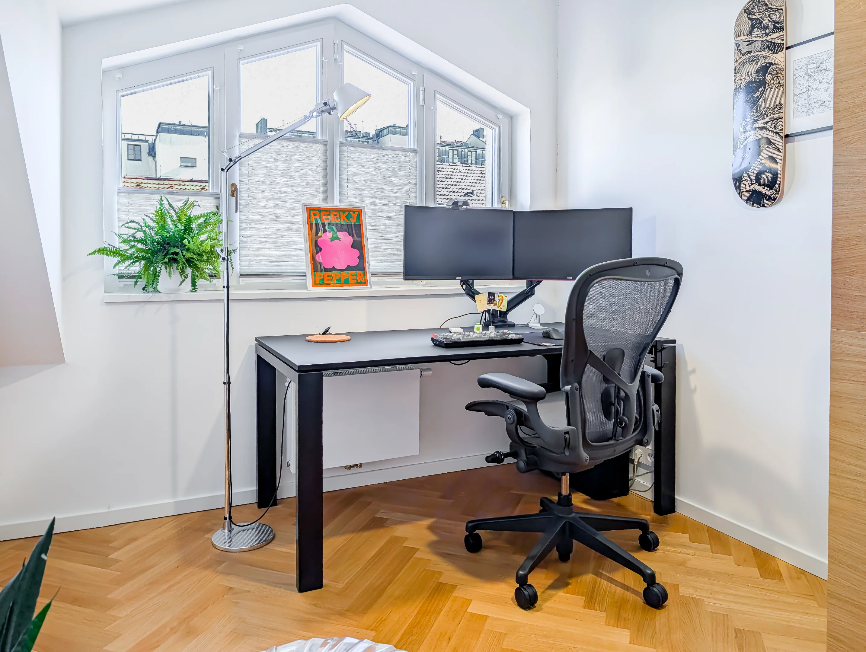 Světlý pokoj s pracovním stolem, monitory a ergonomickou židlí.